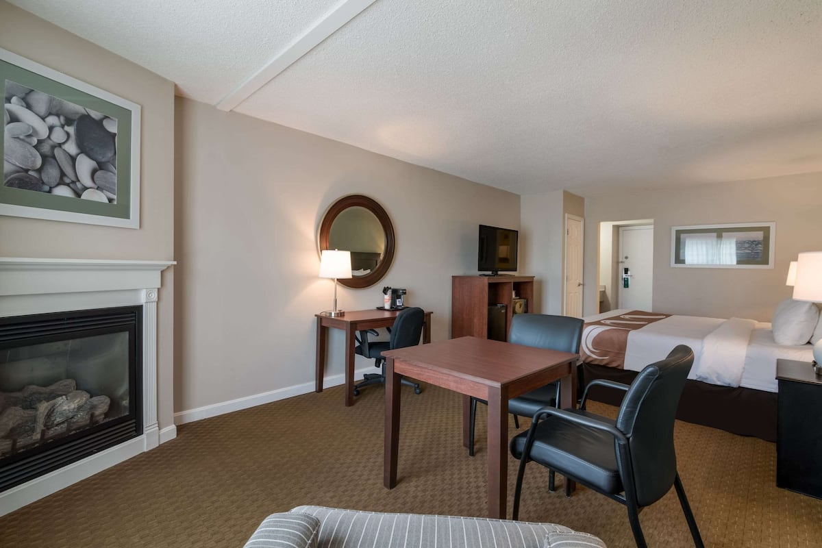 Quarto de hotel com lareira, mesa de jantar com cadeiras, cama e escrivaninha com cadeira.