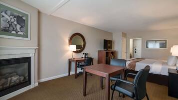 Une chambre d’hôtel avec une cheminée, une table à manger avec des chaises, un lit et un bureau avec une chaise.