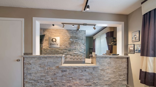 Un área de recepción con pared de piedra, un cartel que dice “Quality by Choice Hotels” y una alfombra roja con el texto “EconoLodge”.