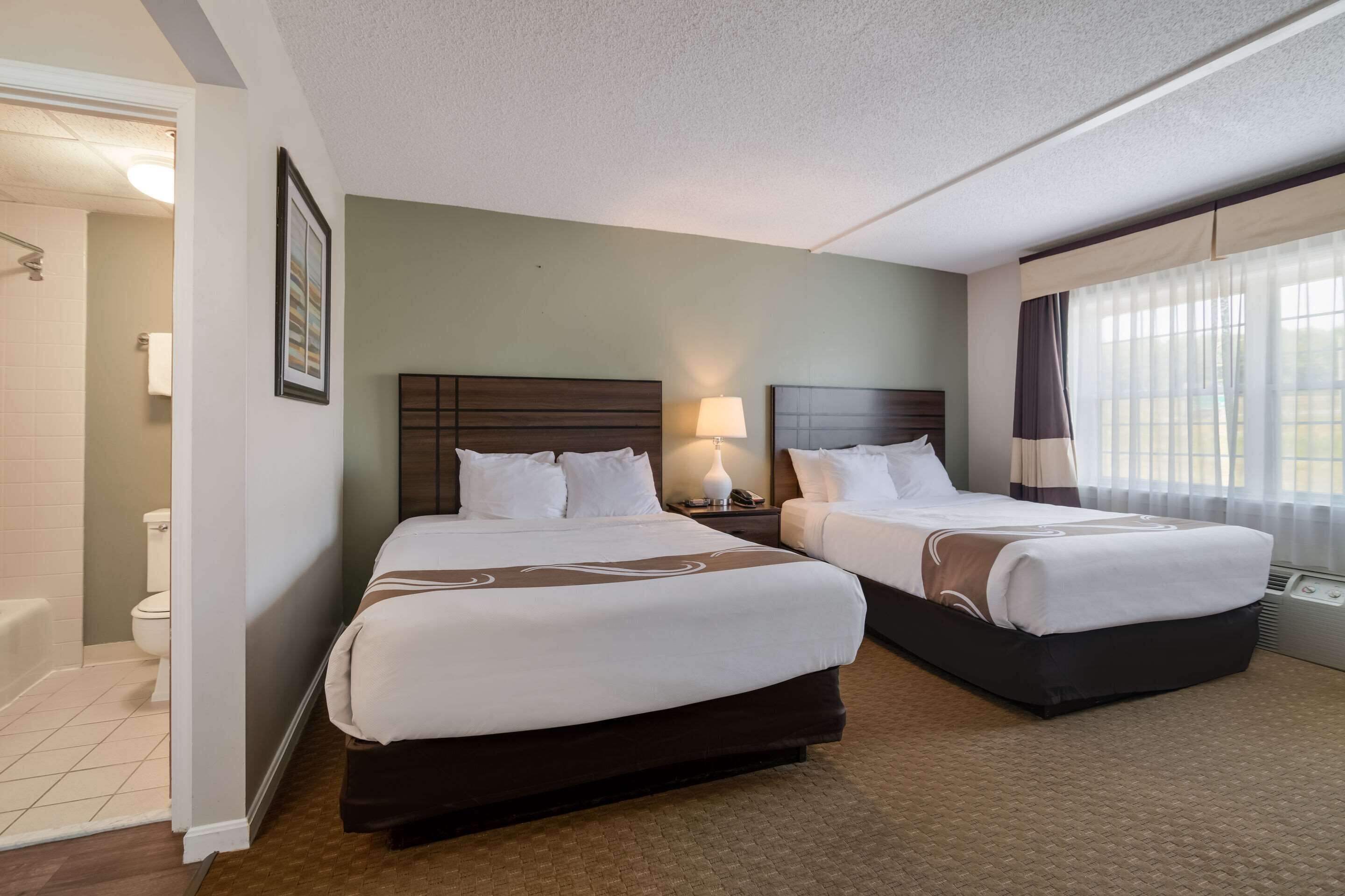 Une chambre d’hôtel avec deux lits, une salle de bain et une fenêtre avec des rideaux.