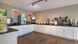 A kitchen with white cabinets, a microwave, a coffee machine, and various food items on the counter.