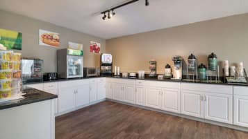 A kitchen with white cabinets, a microwave, a coffee machine, and various food items on the counter.