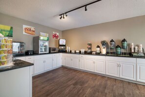 A kitchen with white cabinets, a microwave, a coffee machine, and various food items on the counter.