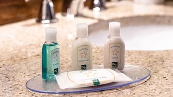 A bathroom counter with three bottles of O Shower products: shampoo, conditioner, and lotion.