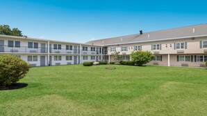 A multi-story hotel with a courtyard featuring a lawn, small trees, and a circular water feature.