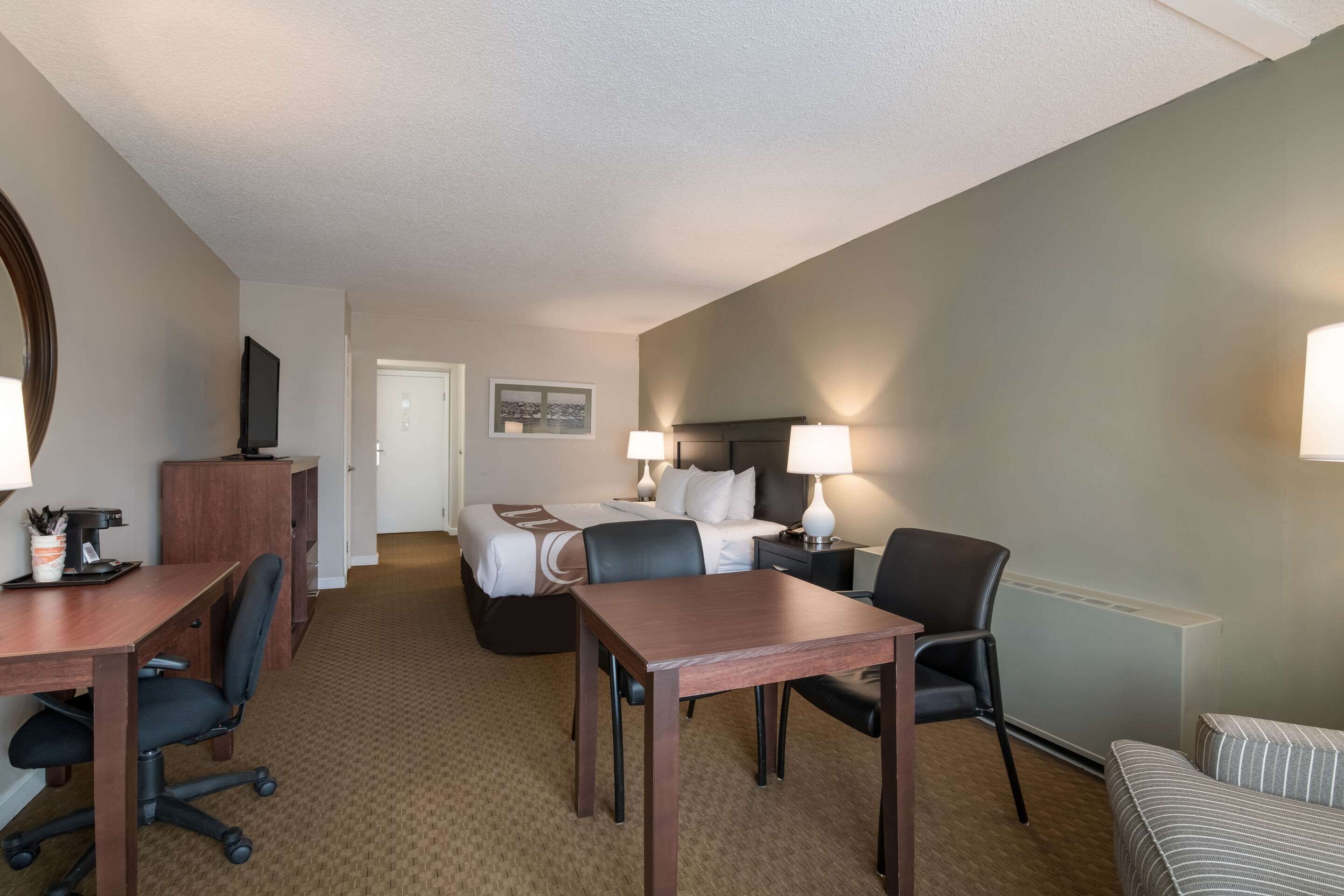 A hotel room with a bed, a desk with a chair, a small table, a sofa, and a TV.