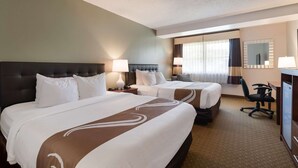 A hotel room with two beds, a desk, a chair, and a large window with curtains.