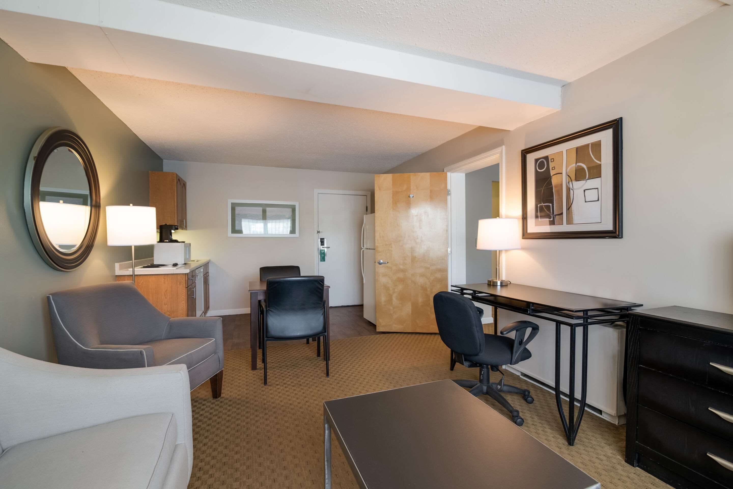 Habitación de hotel con cama, escritorio, dos sillas, lámpara, espejo y un cuadro en la pared.