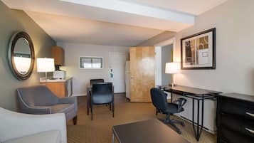 A hotel room with a bed, a desk, two chairs, a lamp, a mirror, and a framed picture on the wall.