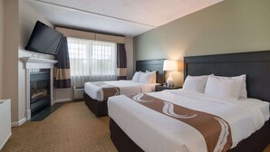 Habitación de hotel con dos camas, un televisor de pantalla plana montado en la pared, chimenea y mesita de noche con lámpara.