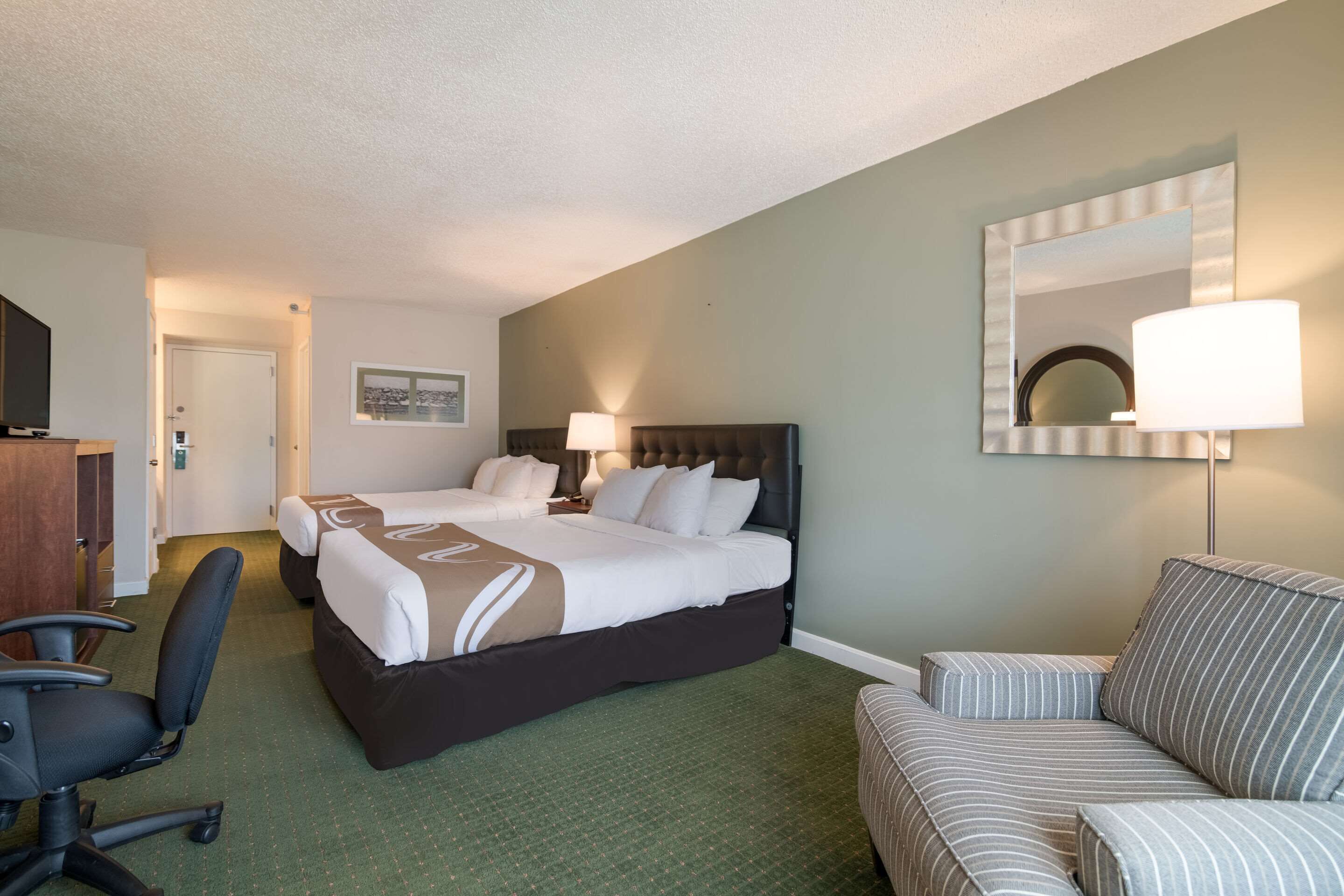 Habitación de hotel con una cama grande, un escritorio, una silla, un sofá y un espejo.