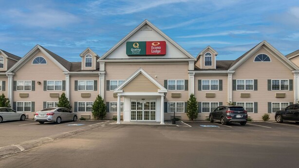 A multi-story hotel with a central entrance, parking lot, and a clear sky.