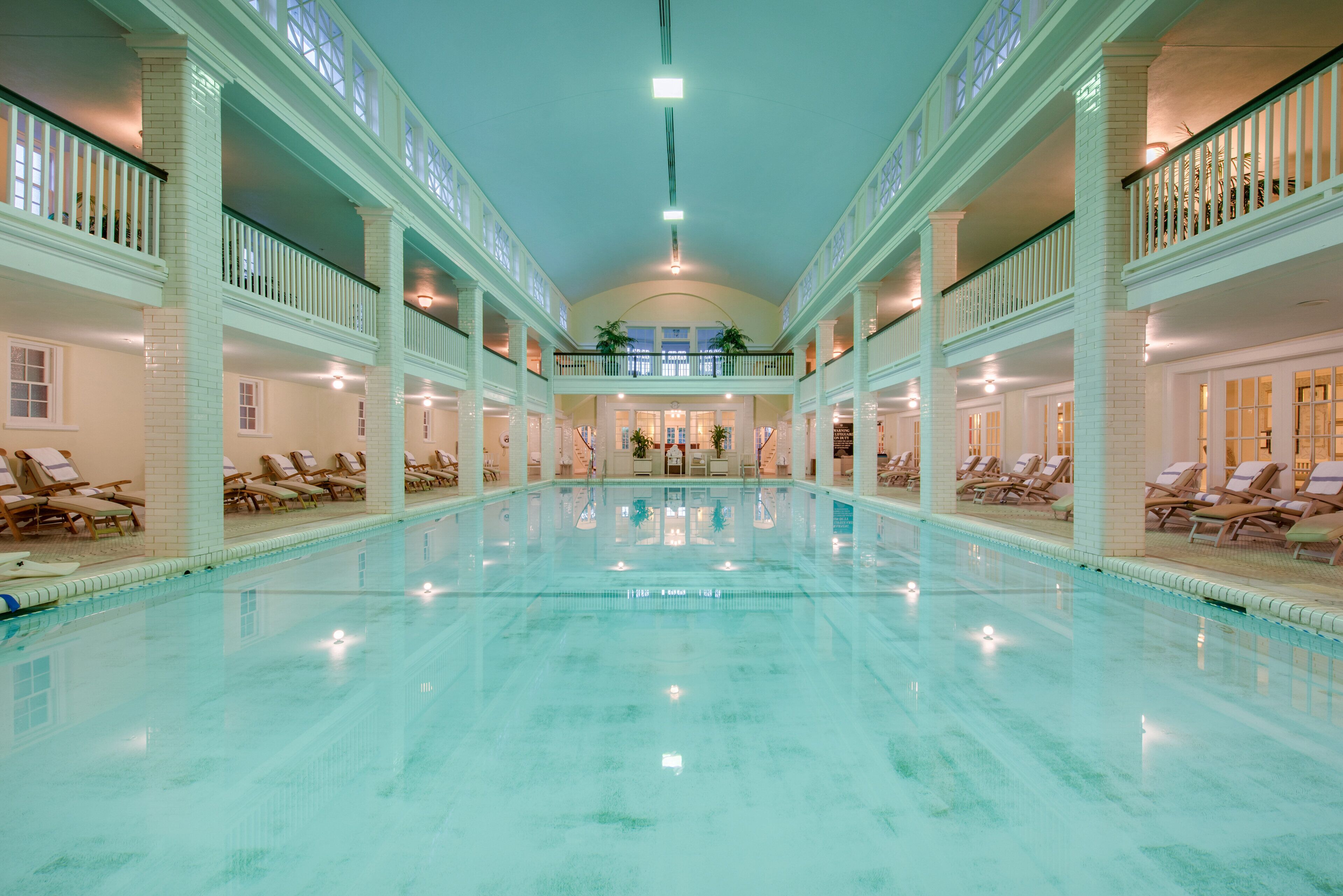 A large indoor swimming pool with multiple levels of balconies and lounge areas.