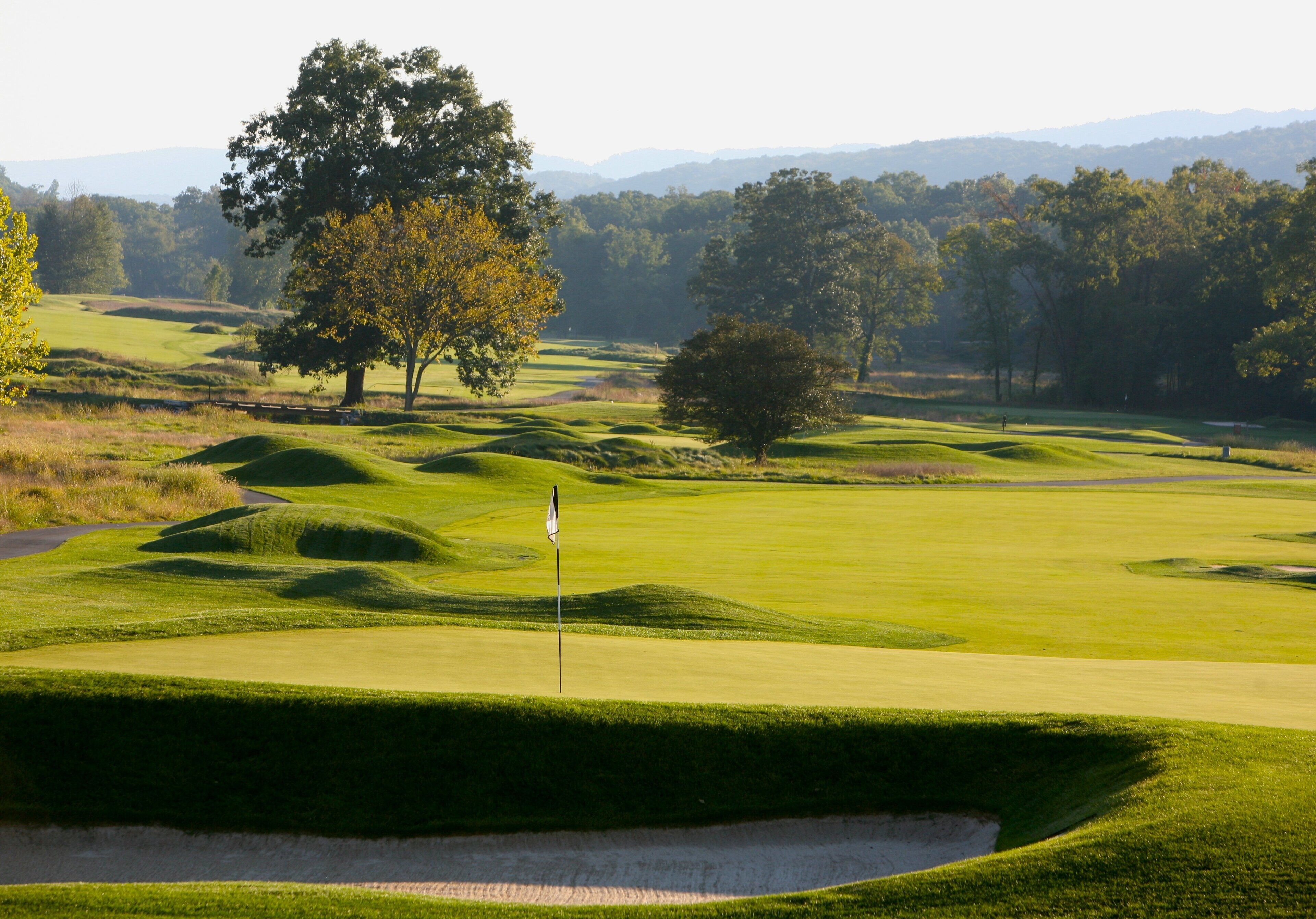 Un parcours de golf avec des collines verdoyantes, des bunkers de sable et un mât de drapeau.
