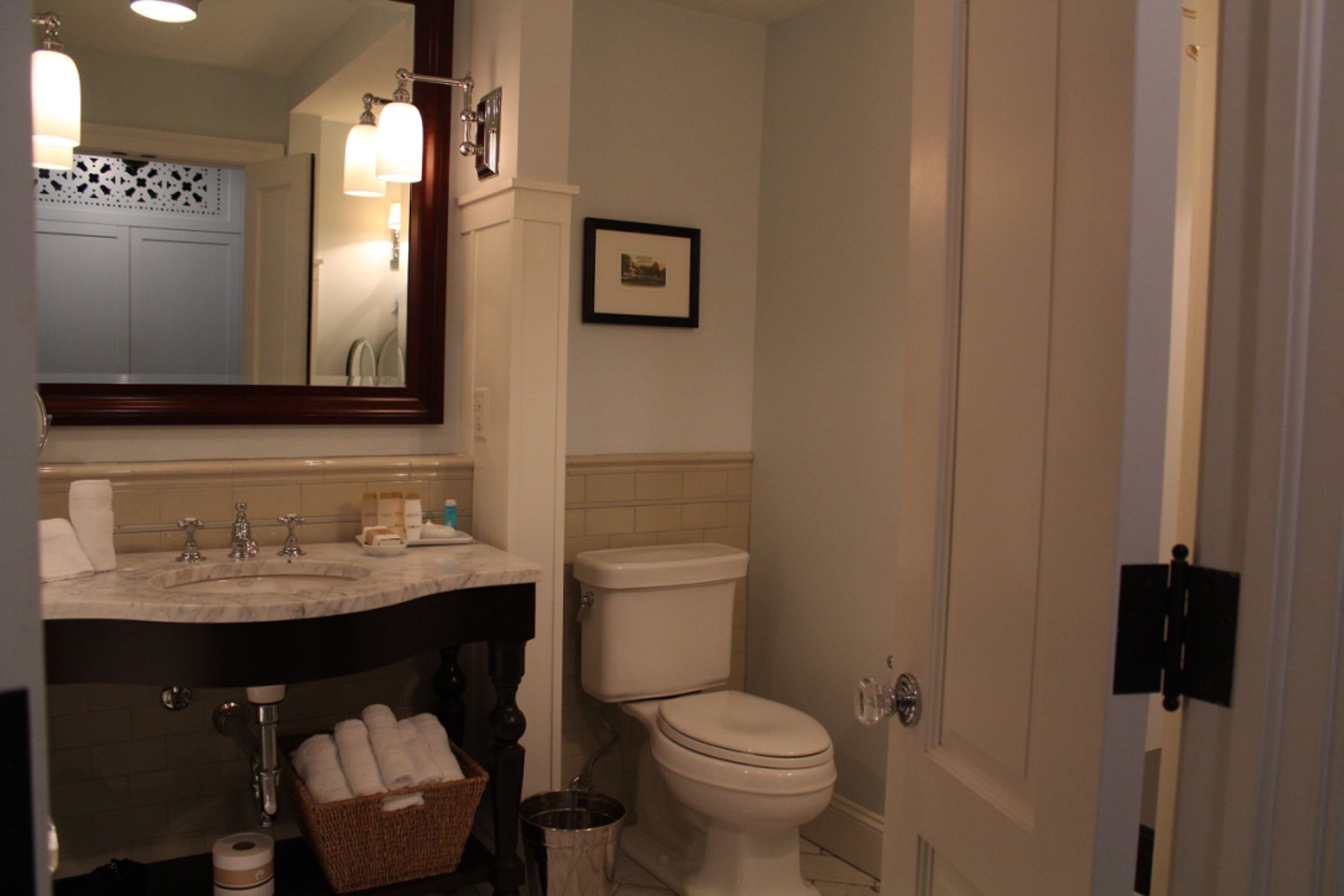 A bathroom with a sink, mirror, toilet, and a framed picture on the wall.