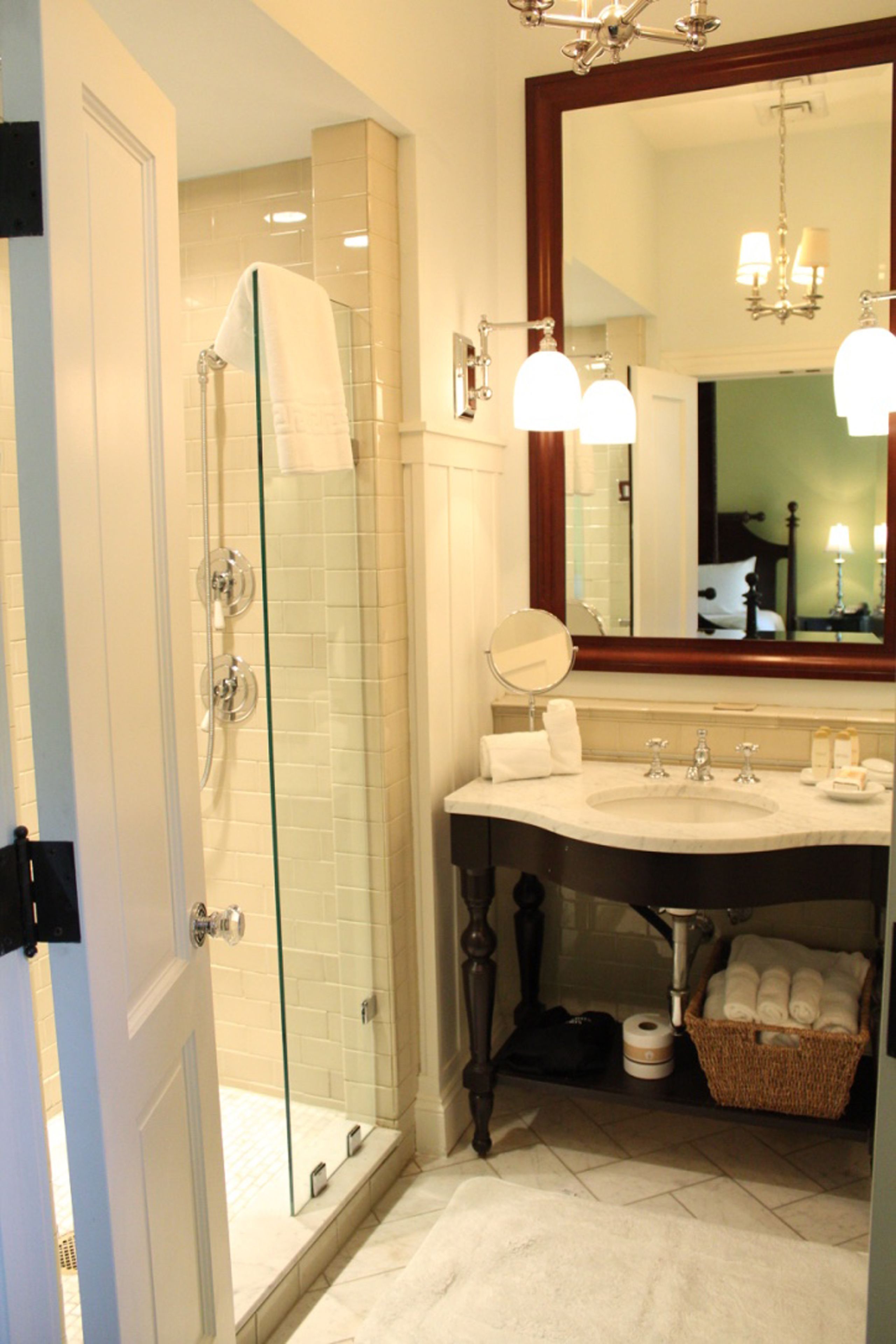 A bathroom with a glass-enclosed shower, a vanity with a mirror, and a chandelier above the mirror.