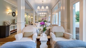 Un salon spacieux avec deux canapés placés face à une table basse centrale, un lustre et de grandes fenêtres.