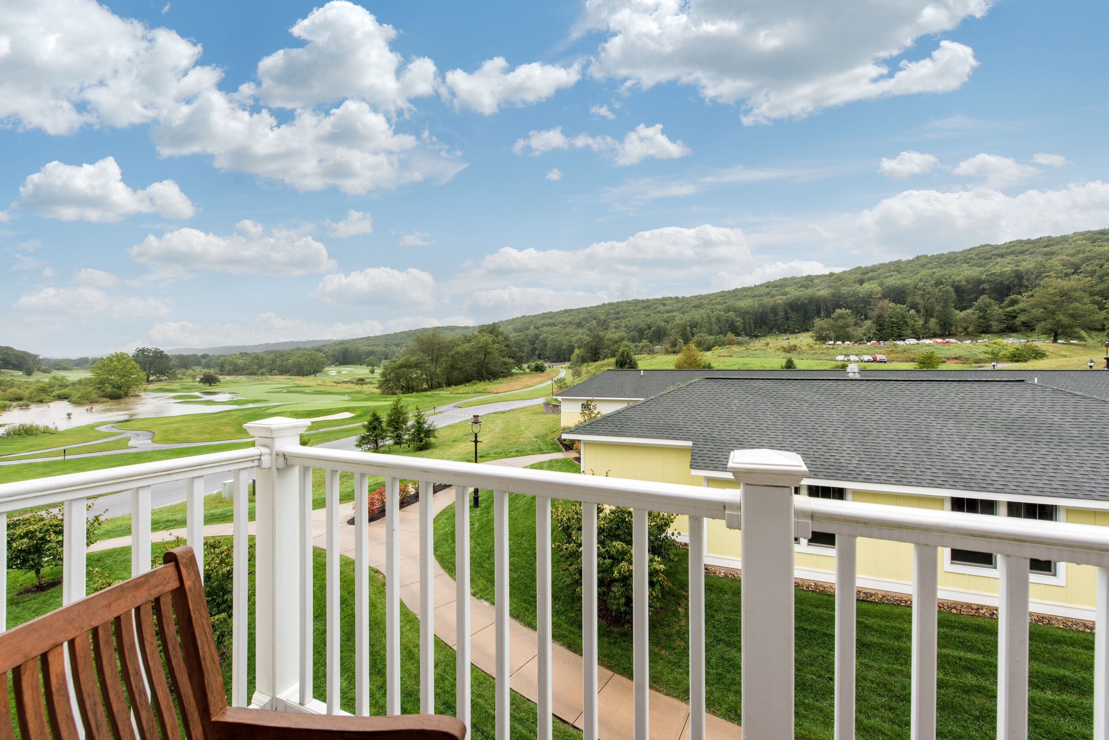 Ein Balkon mit Blick auf einen Golfplatz, ein gelbes Gebäude und einen grünen Hügel.