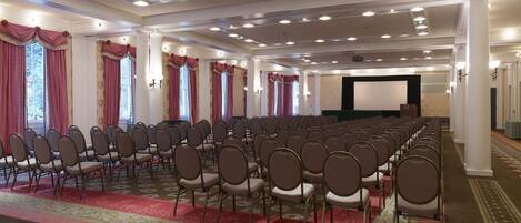 A conference room with rows of chairs, a stage, and a projector screen.