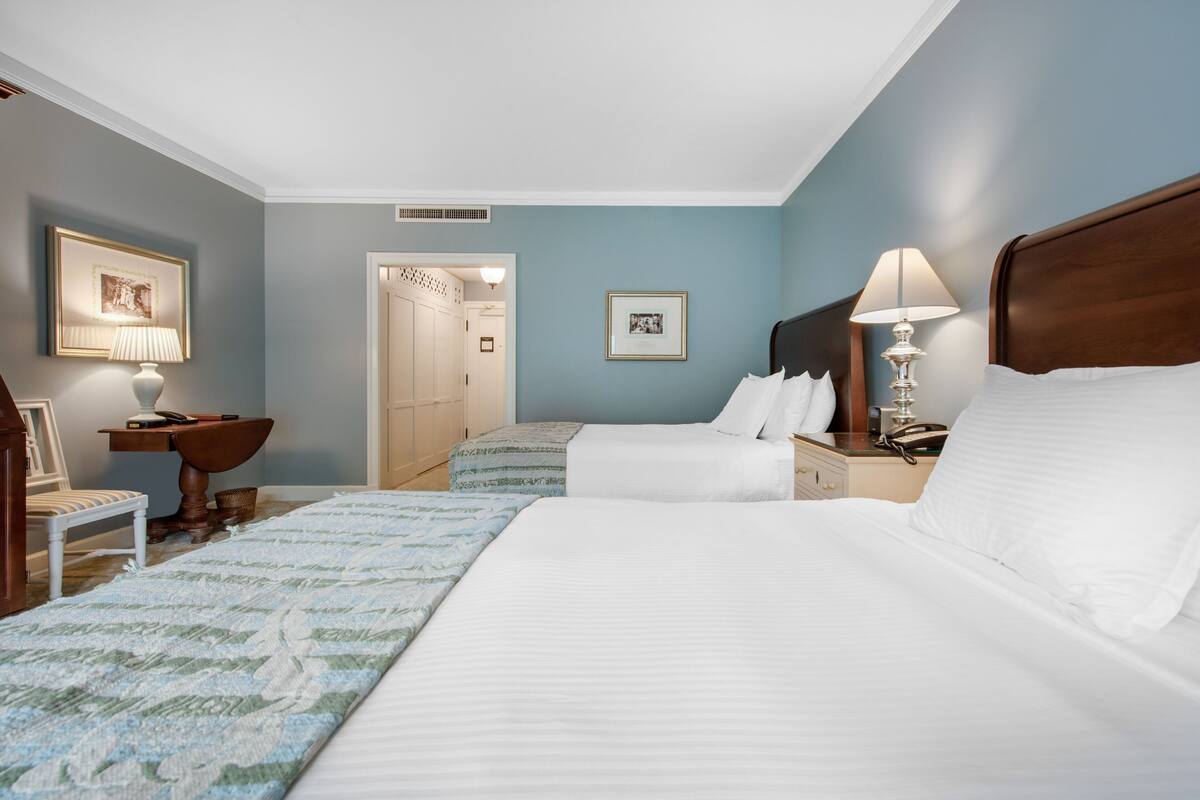 Ein Hotelzimmer mit zwei Betten, einem Schreibtisch, einem Stuhl und einem Nachttisch mit Lampen.