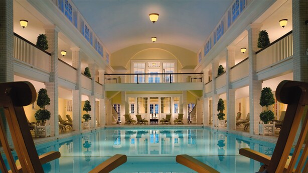 Un espace piscine aménagé avec des chaises longues et une table, entouré de murs en briques blanches et de nombreux balcons.