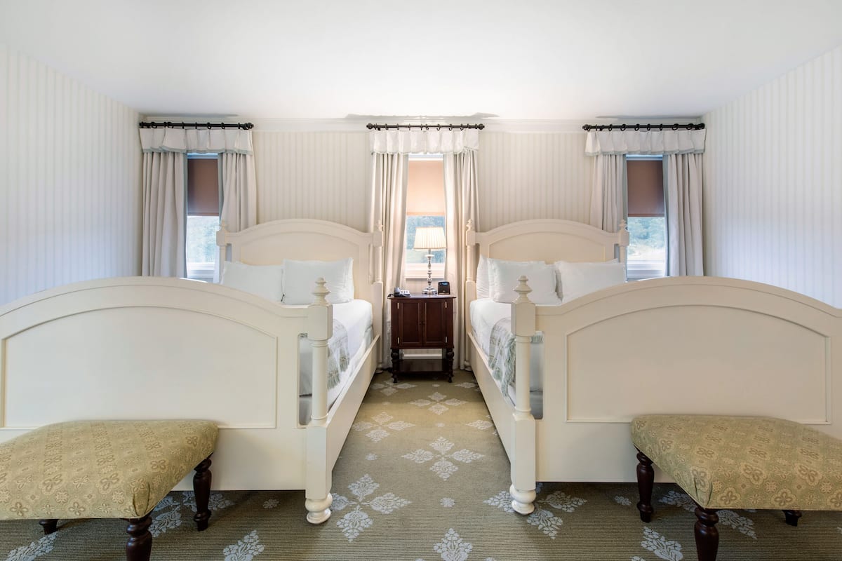 Ein Hotelzimmer mit zwei Einzelbetten, einem kleinen Tisch und einer Bank.