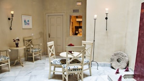 Una habitación con una mesa redonda, cuatro sillas de madera con cojines estampados, una pequeña mesa redonda con un florero y un espejo en la pared.