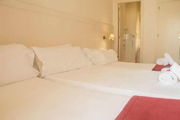 Habitación de hotel con una cama grande, baño con ducha y cama bien hecha con toallas.