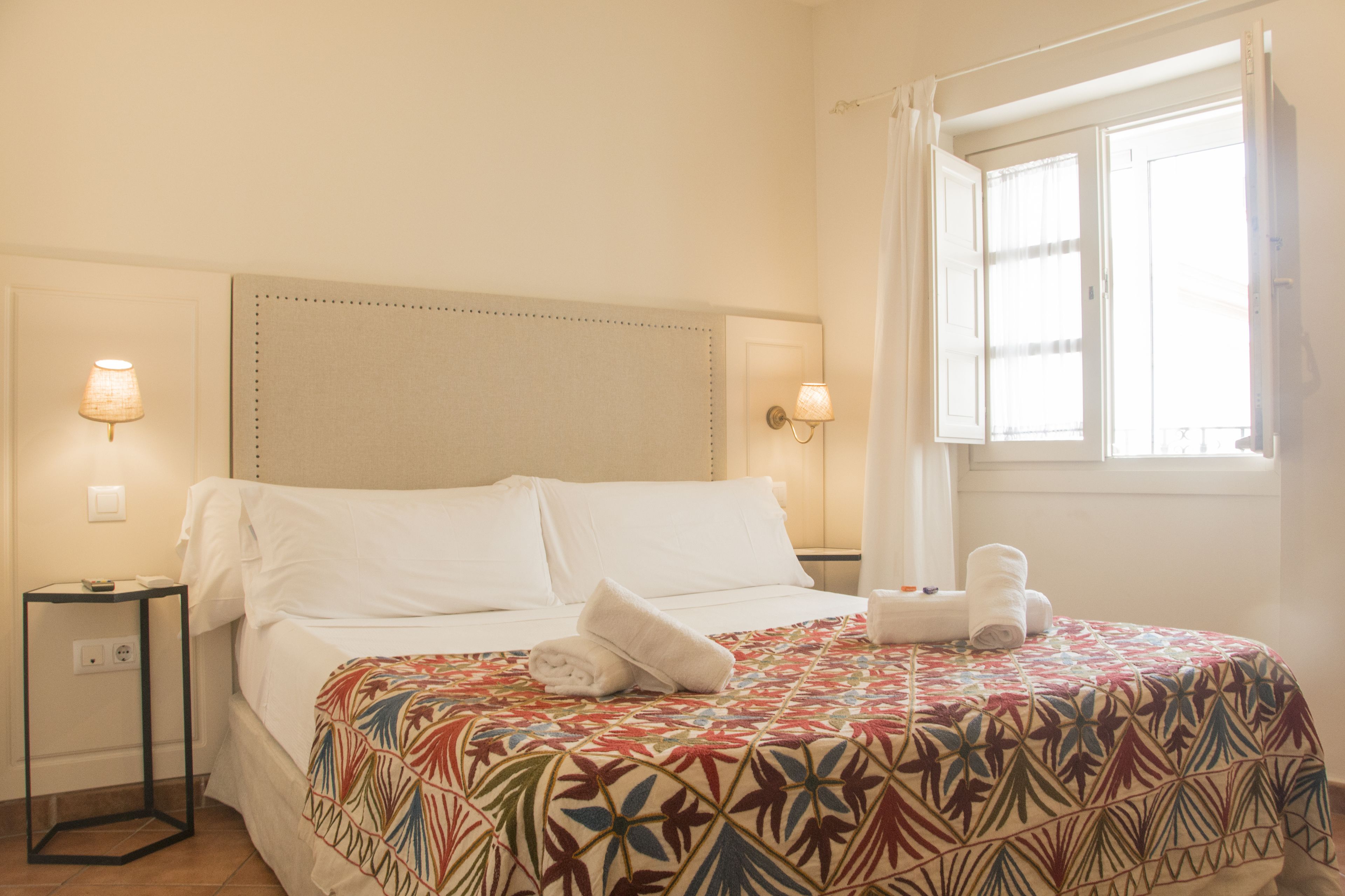 Une chambre d’hôtel avec un lit, deux lampes de chevet, une fenêtre avec des rideaux et une couvre-lit à motifs.