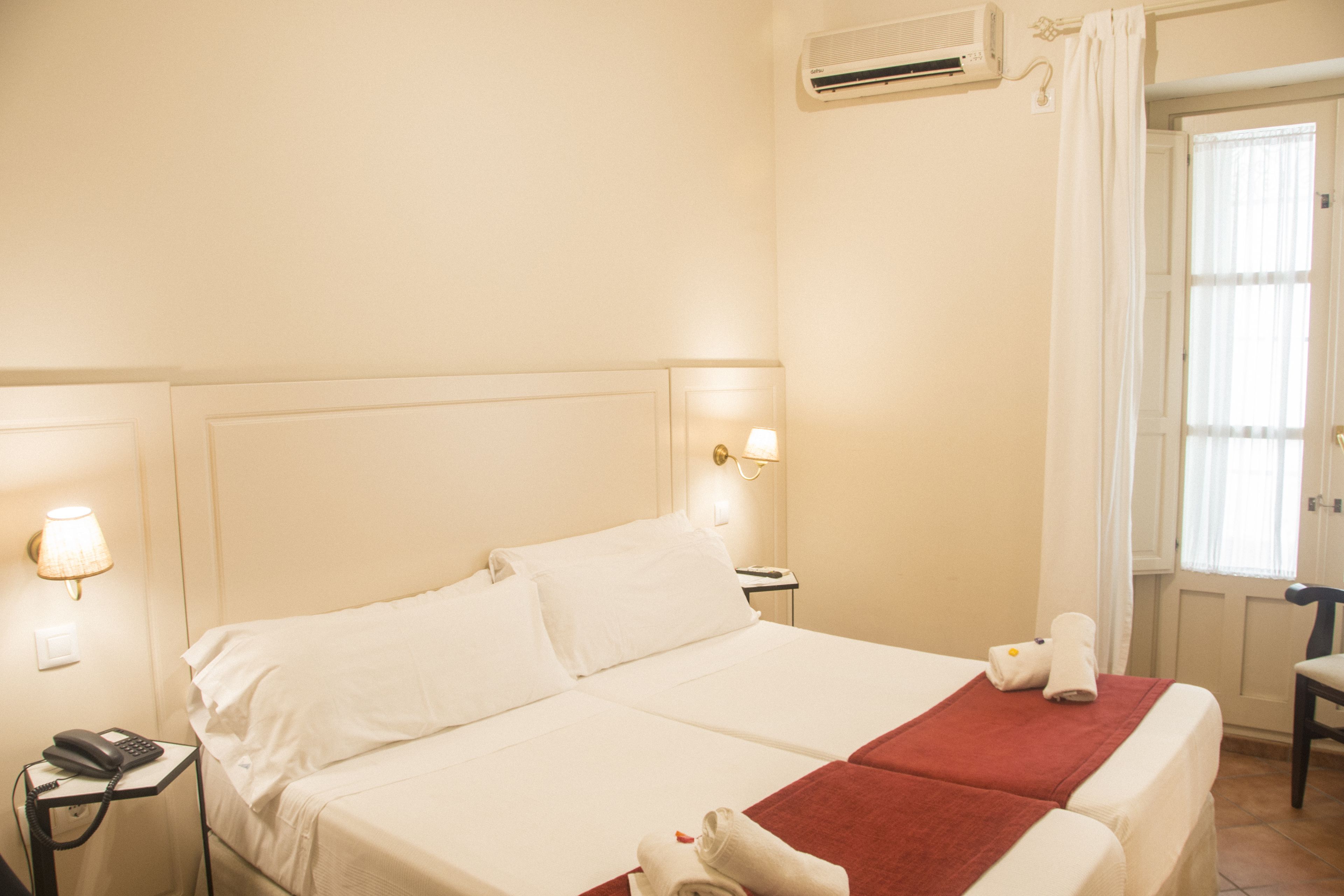 A hotel room with a large bed, bedside lamps, a telephone, and a window with curtains.