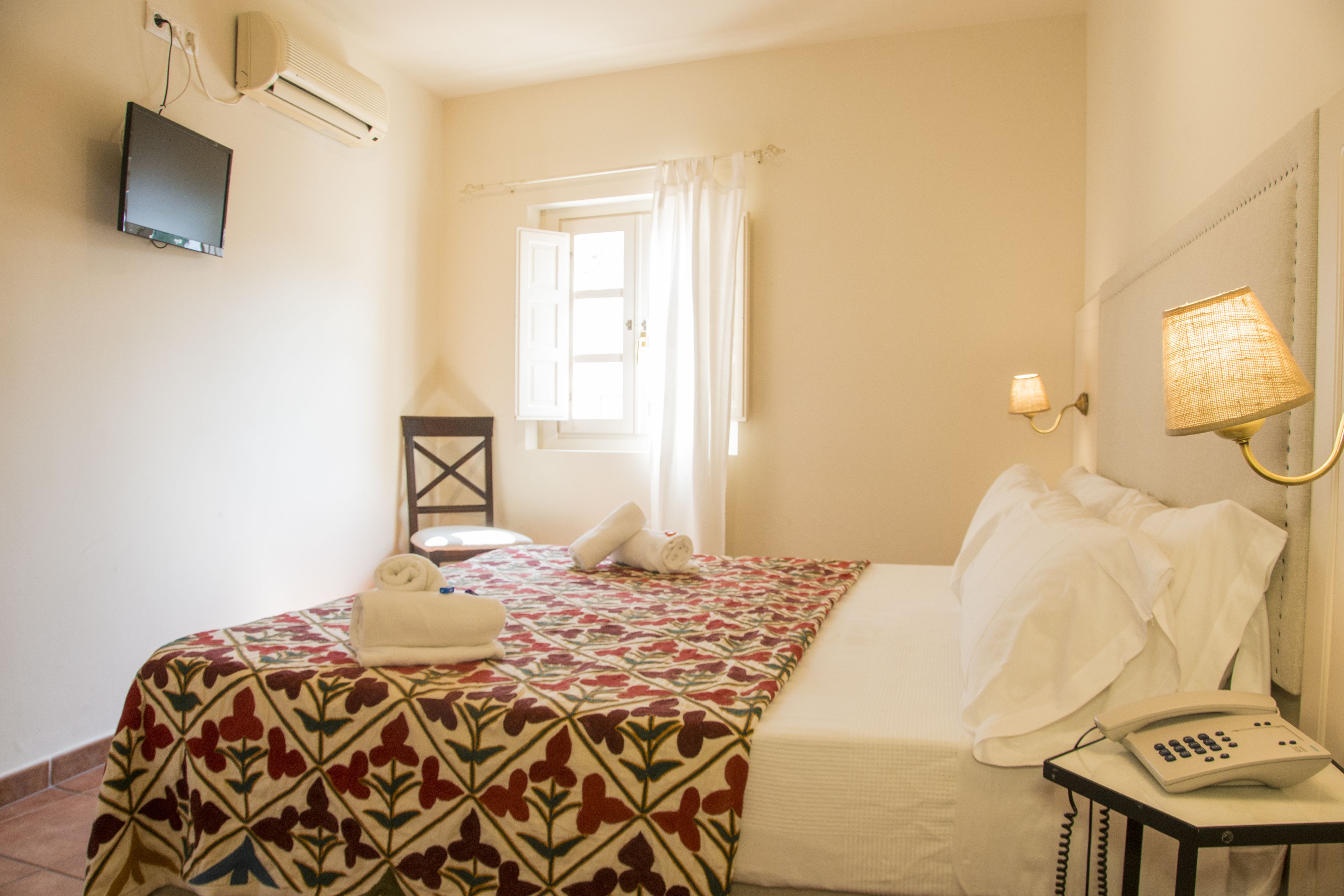 Une chambre d’hôtel équipée d’un lit, d’une lampe de chevet, d’un téléphone, d’une fenêtre avec des rideaux et d’un climatiseur fixé au mur.