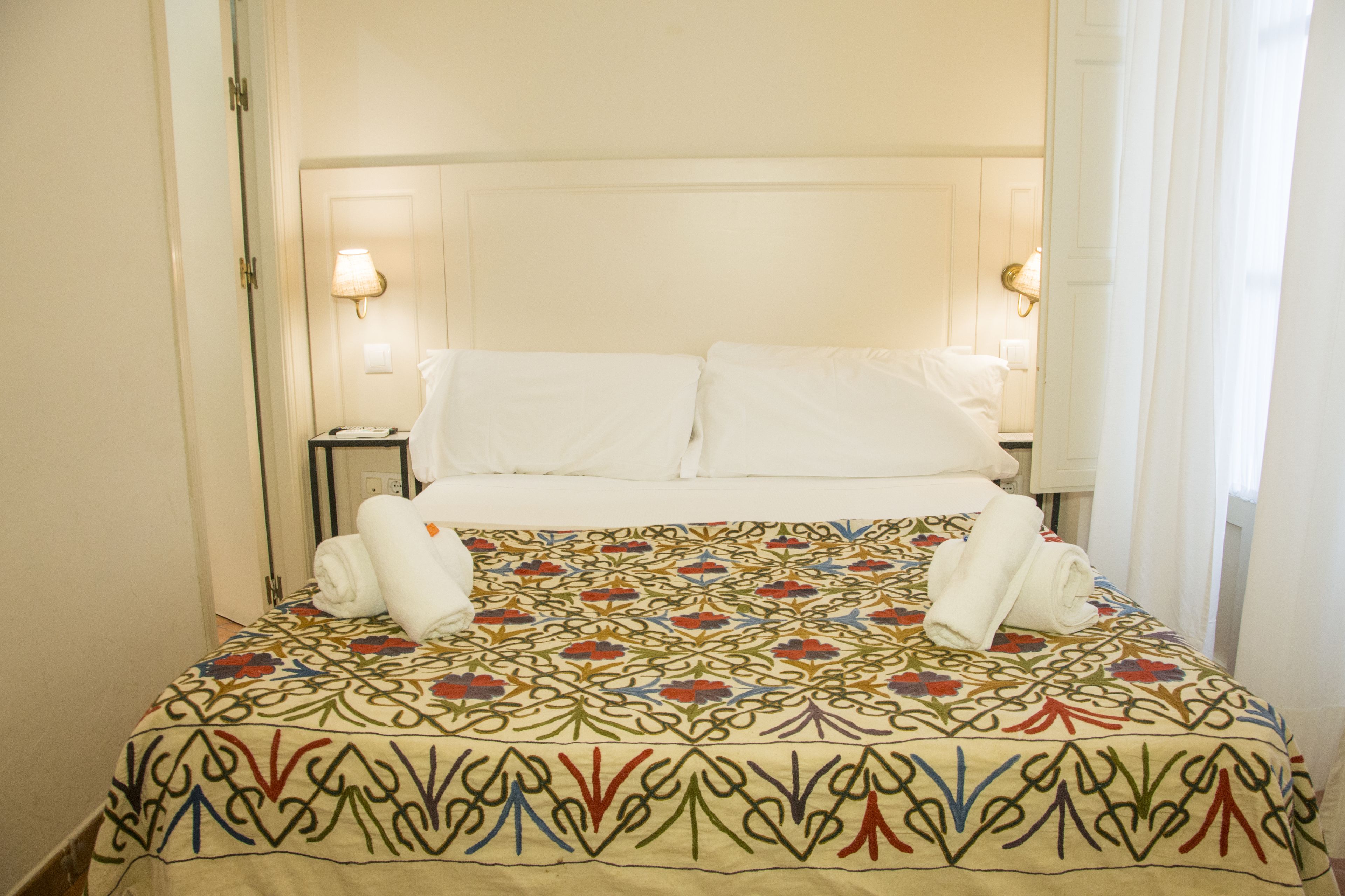A hotel room with a bed, two bedside lamps, and a patterned bedspread.