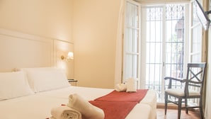 Habitación de hotel con dos camas, una colcha roja, una silla y una ventana con vista a un edificio.