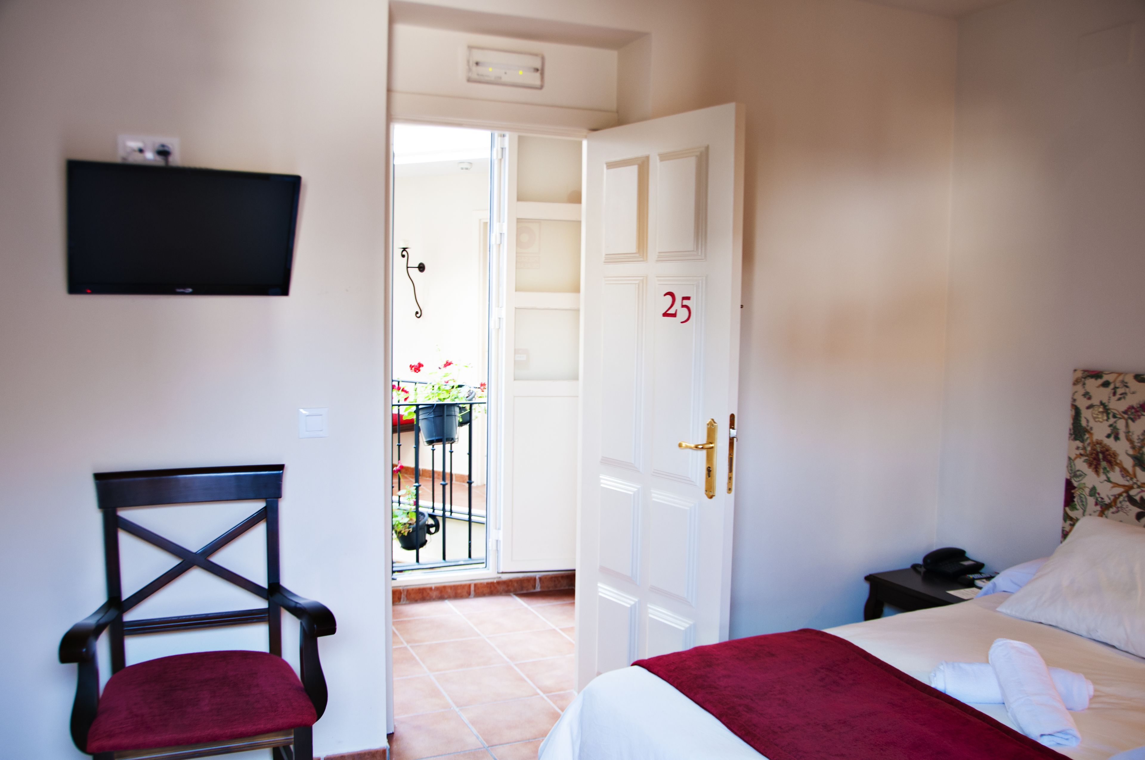 A hotel room with a bed, a chair, a TV mounted on the wall, and a door with the number 25.