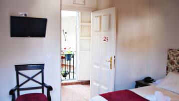 A hotel room with a bed, a chair, a TV mounted on the wall, and a door with the number 25.