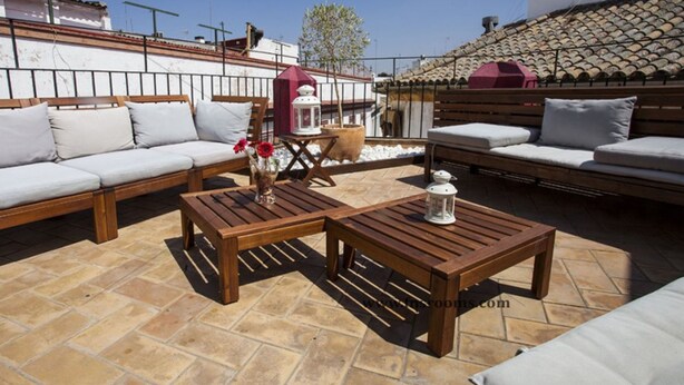 Un patio con muebles de madera, incluyendo un sofá y dos mesas, y una planta en maceta.