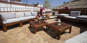 Un patio con muebles de madera, incluyendo un sofá y dos mesas, y una planta en maceta.