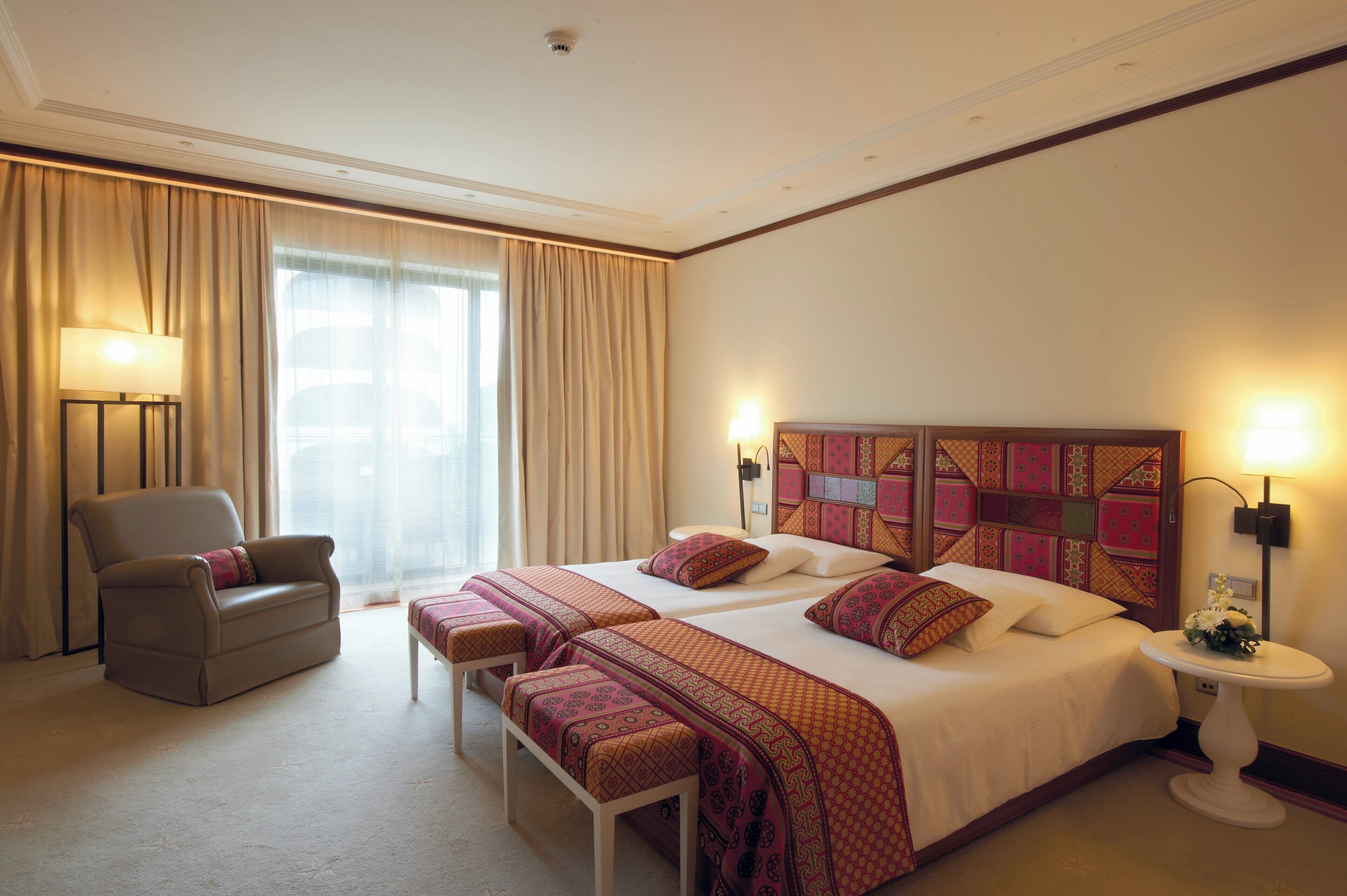 A hotel room with a large bed, two bedside tables, a chair, and a window with curtains.