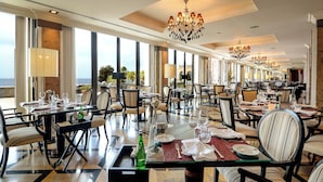 Un comedor amplio con varias mesas y sillas, ventanas grandes que ofrecen vistas al exterior, y elegantes lámparas de araña.