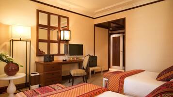 Quarto de hotel com duas camas, uma escrivaninha com computador, uma cadeira, um abajur e um espelho.