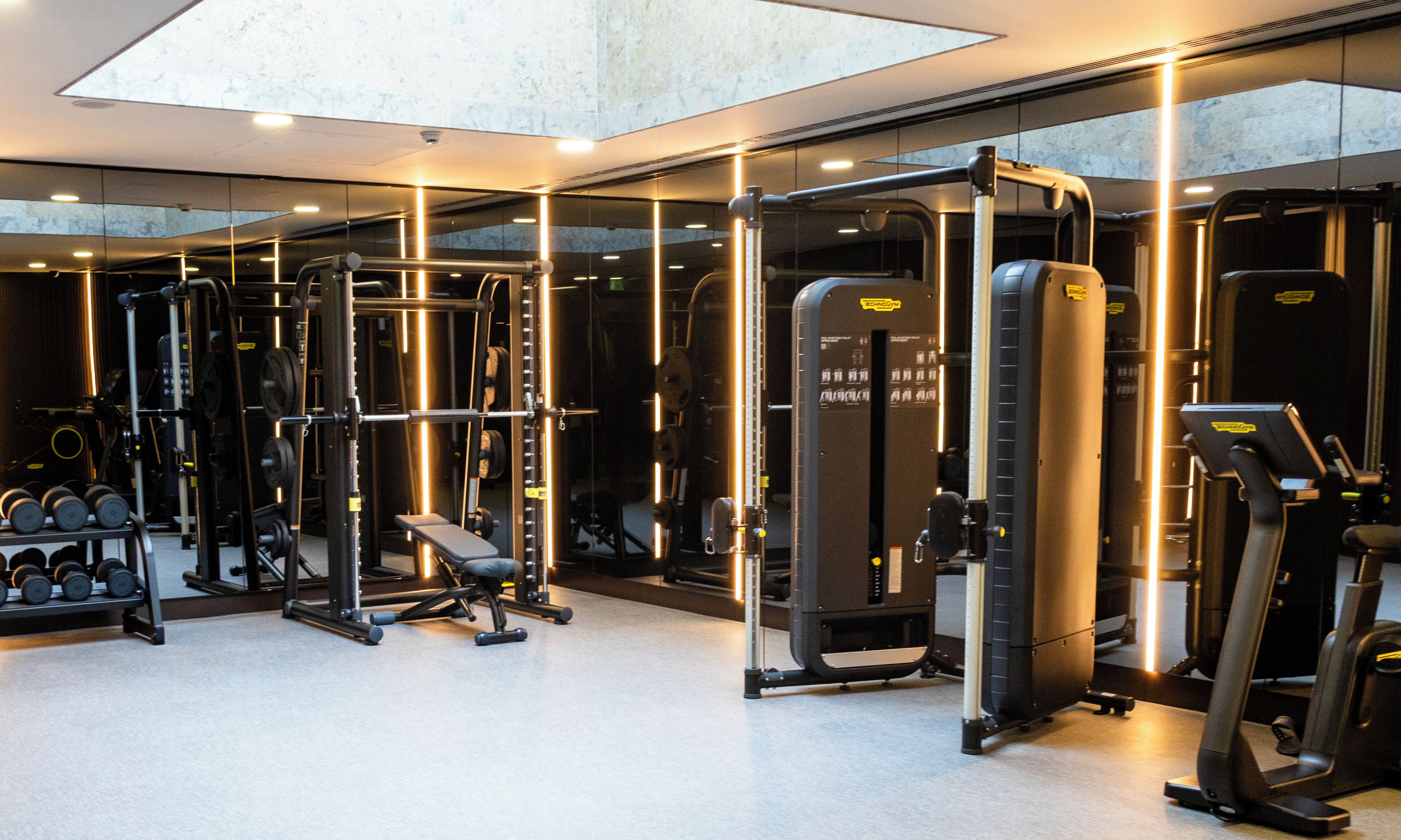 A gym with various exercise equipment, a bench, and a mirrored wall.