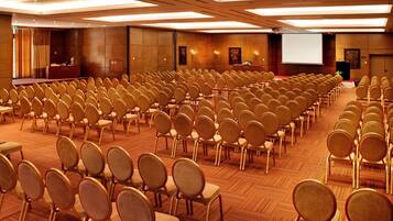 Un amplio salón de conferencias con filas de sillas, un atril y una pantalla.