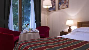 A hotel room with a bed, a red armchair, a table with a vase of flowers, and a lamp.
