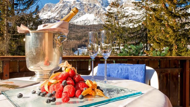 A table with a fruit platter, two wine glasses, and a champagne bottle in a scenic outdoor setting with snow-capped mountains in the background. - Boutique Hotel Villa Blu Cortina (Cortina d'Ampezzo)