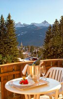 Ein Tisch mit einer Flasche, Weingläsern und einem Teller Essen auf einem Balkon mit Blick auf eine Berglandschaft.