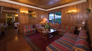 A cozy, wood-paneled living room with a large sectional sofa, a coffee table, and a red rug. - Boutique Hotel Villa Blu Cortina (Cortina d'Ampezzo)