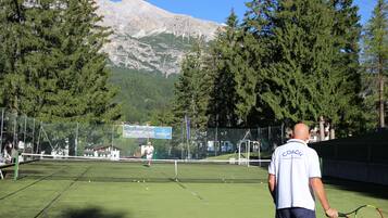 Una cancha de tenis con una red, rodeada de árboles y una montaña al fondo.