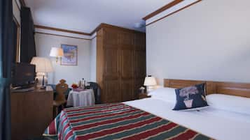 Quarto de hotel com uma cama, escrivaninha com luminária, guarda-roupa e televisão.
