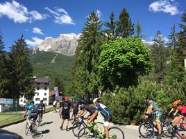 A group of cyclists in a mountainous area with a building in the foreground.