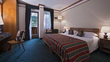 Habitación de hotel con cama, escritorio, silla, mesita de noche y ventana con cortinas.